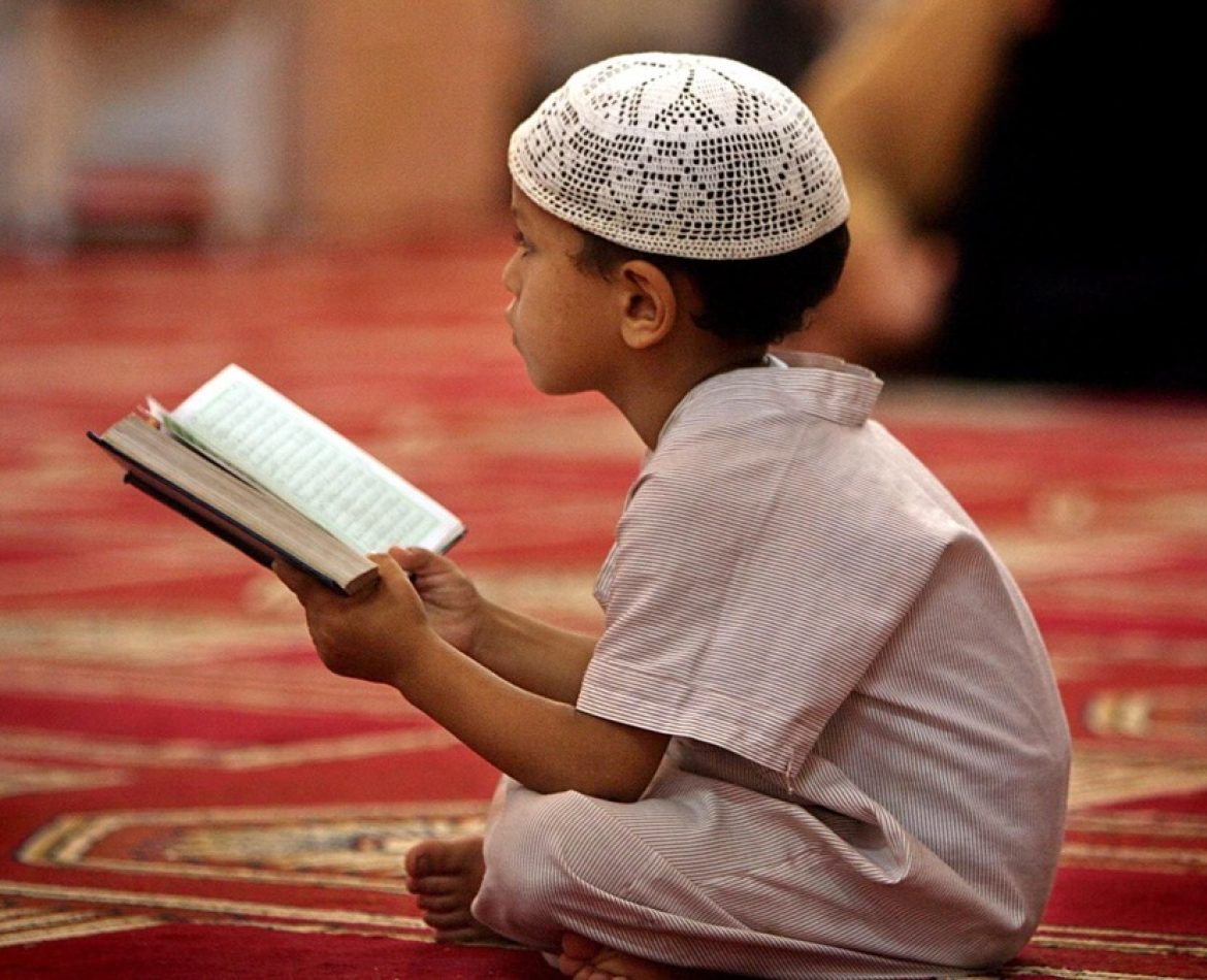 Muslim child reading the Quran in Arabic inside a mosque